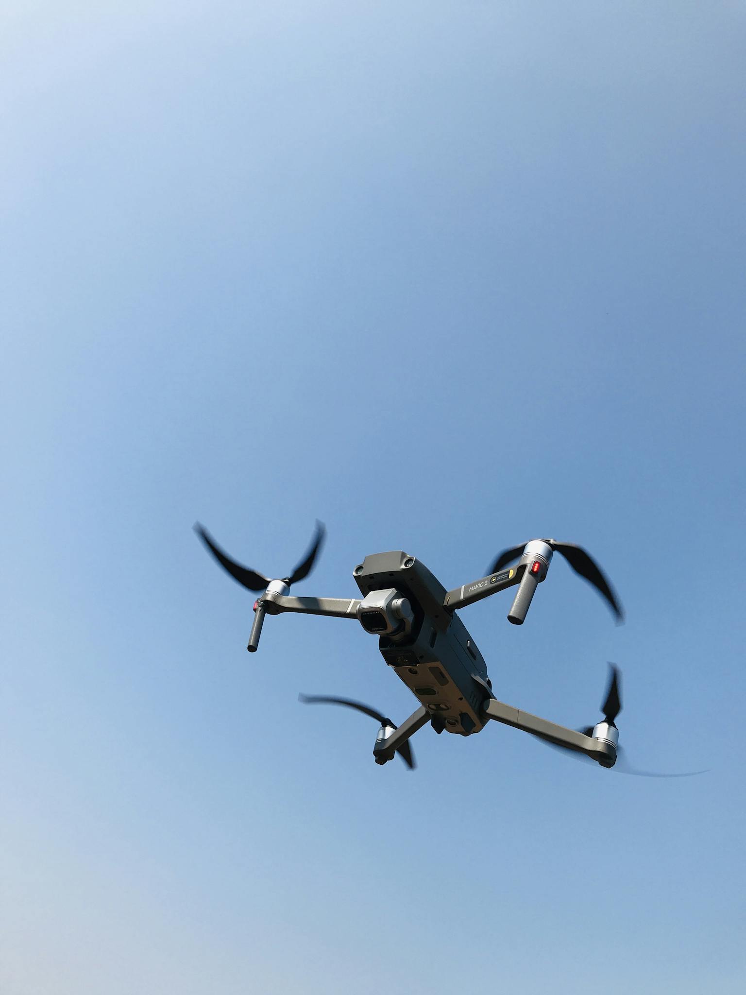 A flying drone captured from below against a clear blue sky in Nallambakkam, India.
