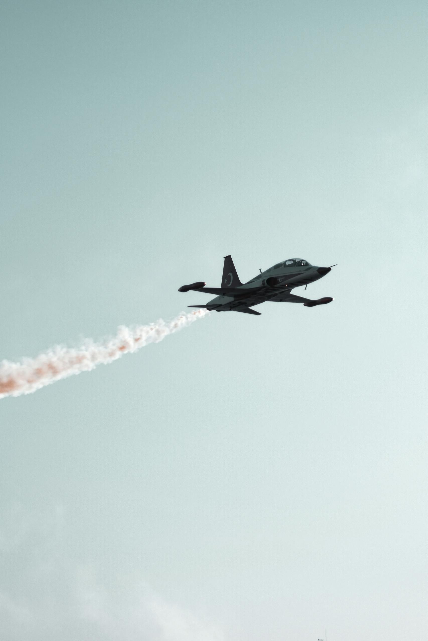 A military jet with contrail performing stunning aerial acrobatics against a clear sky.